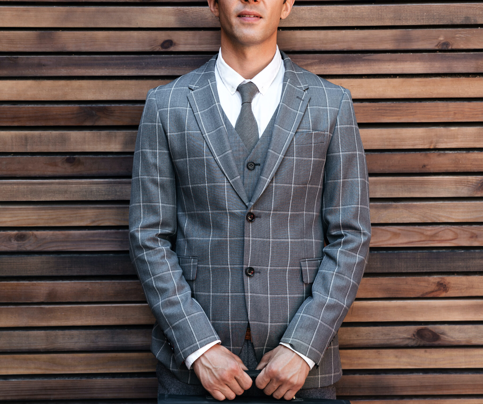 Handsome businessman in suit standing with briefcase against wooden wall background and looking at camera