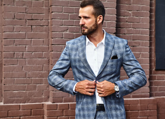 Portrait of sexy handsome fashion businessman model dressed in elegant checkered suit posing on street background. Metrosexual