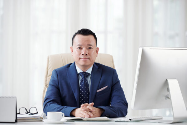 Successful confident Vietnamese businessman sitting at his office table and looking at camera