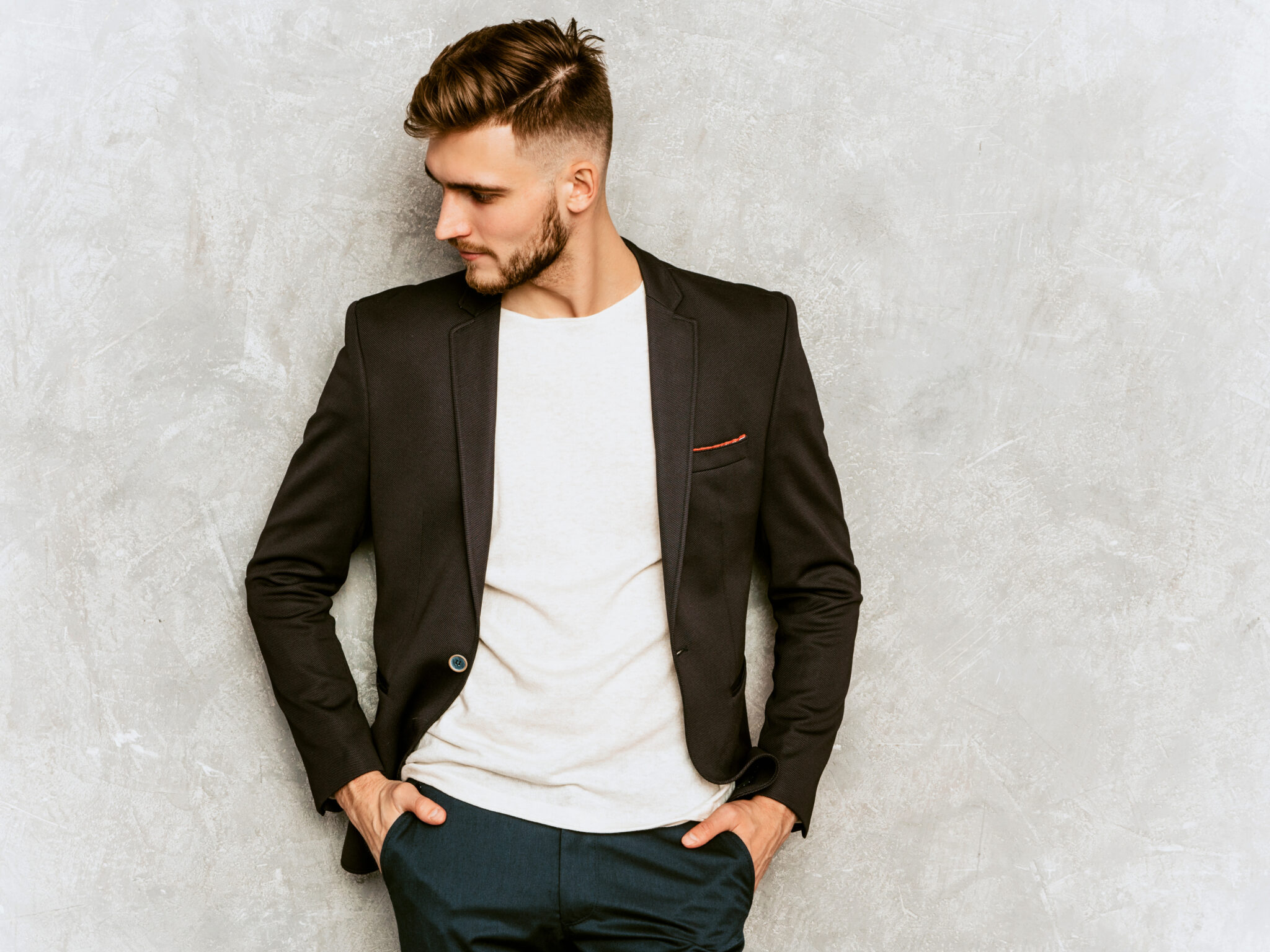 Portrait of handsome hipster lumbersexual businessman model wearing casual black suit. Fashion stylish man posing against gray wall